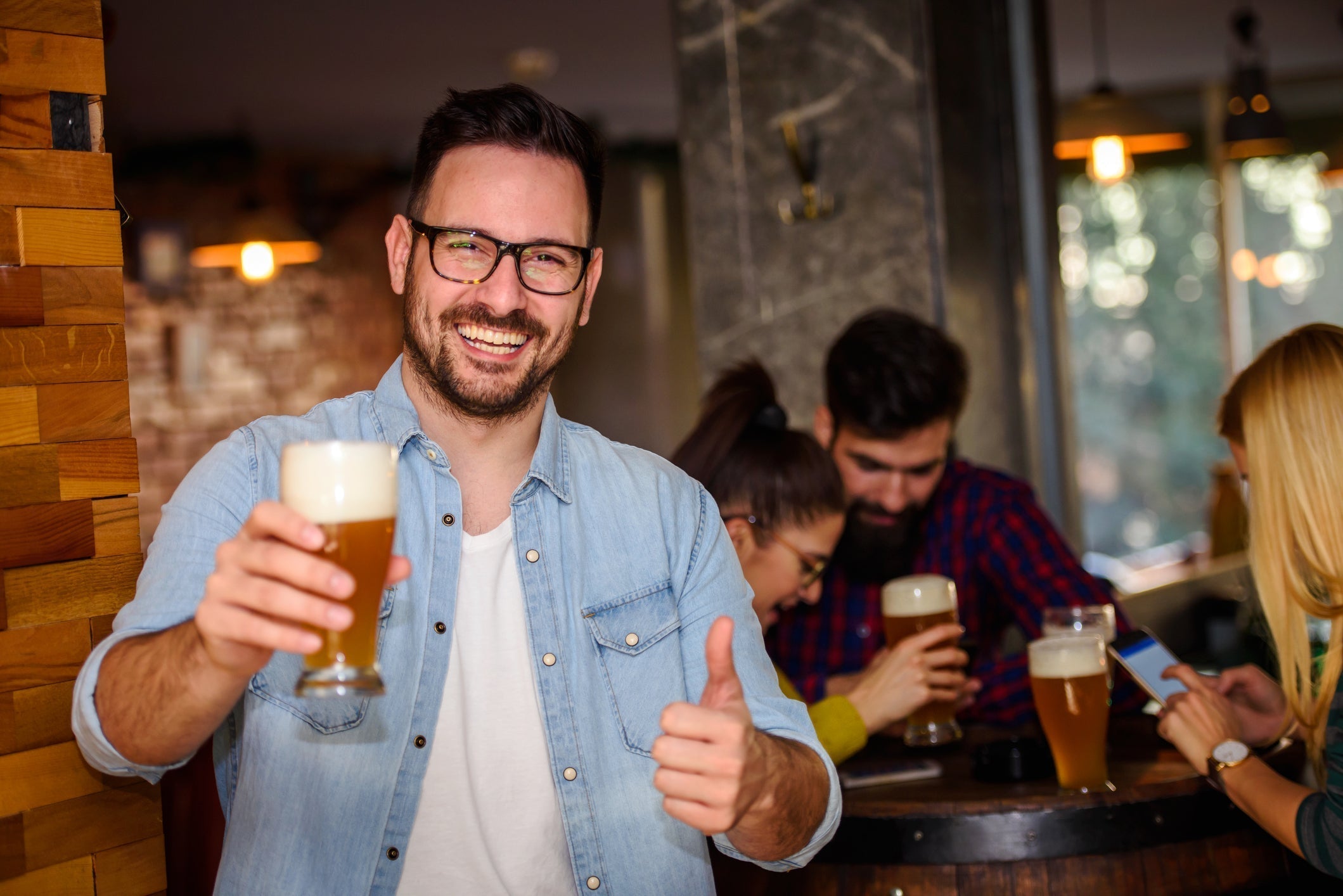 Happy man holding beer in pub with thumbs up
