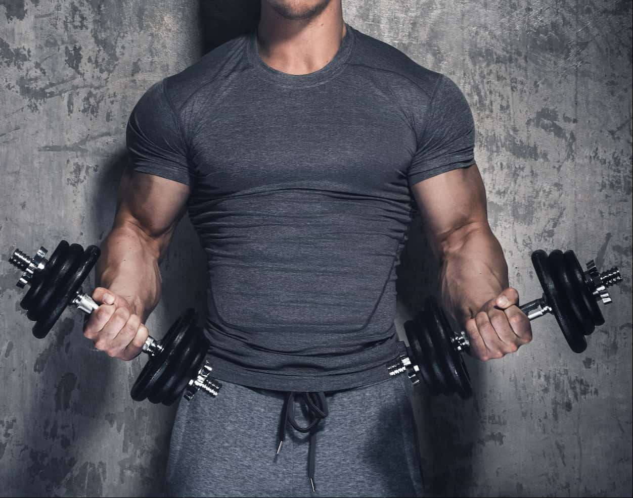 Man with large muscles holding weights against grey wall